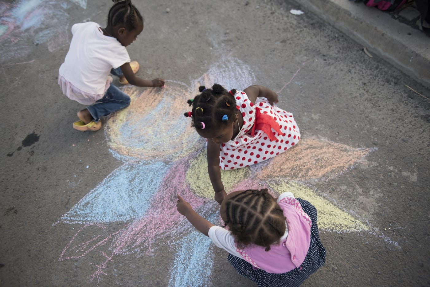 Three children doing a colorful painting on the asphalt