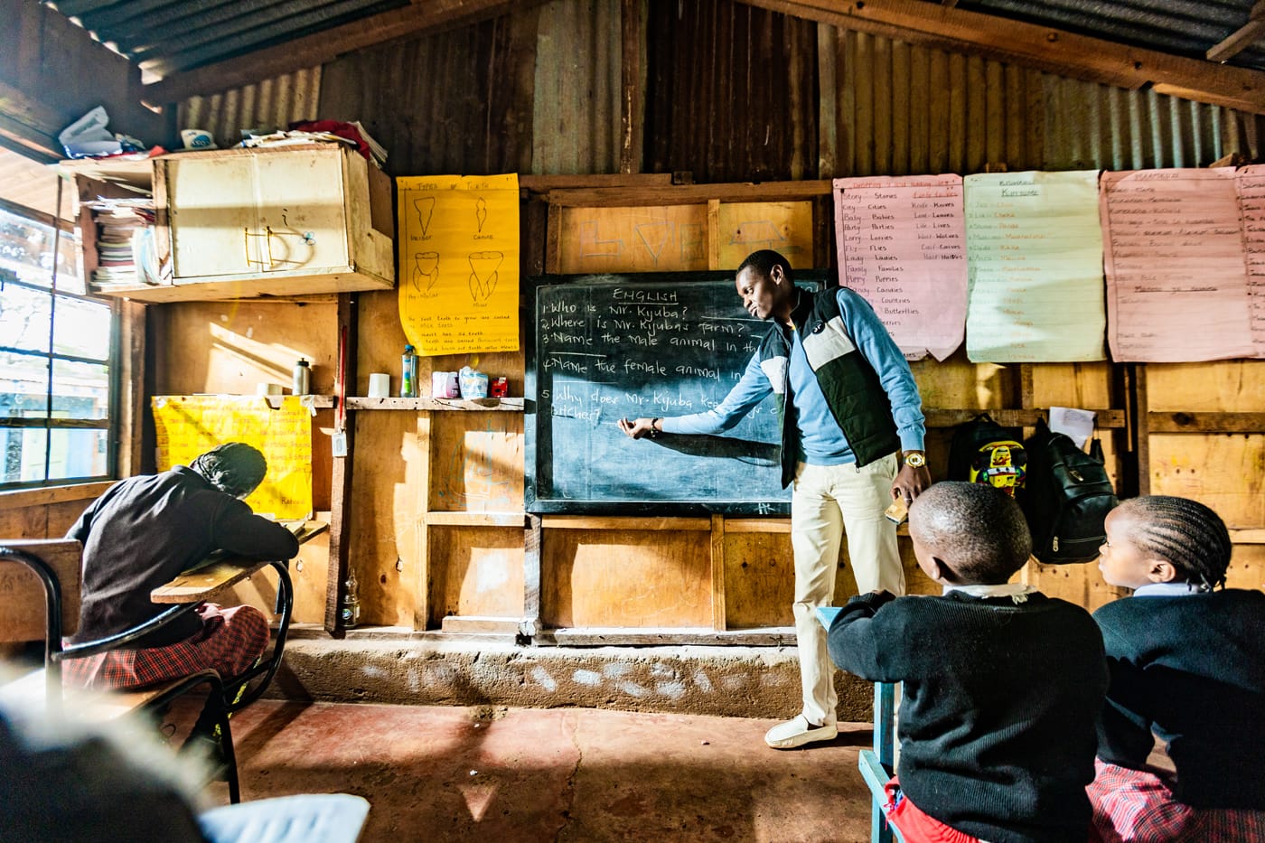 A school teacher in front of his class showing text on a black board