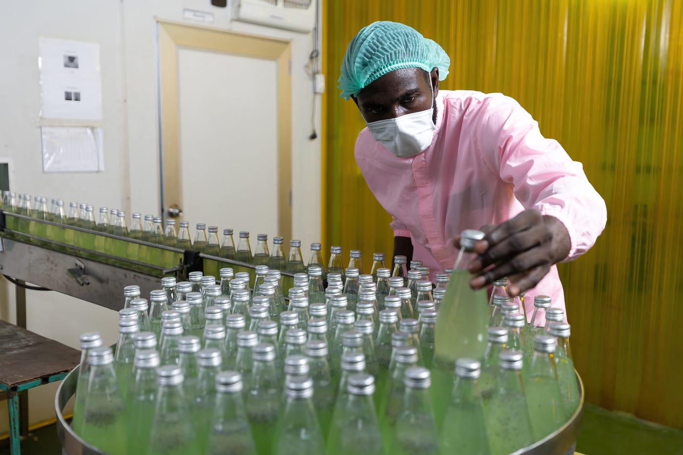 Man in a protective mask checking bottles on a bottling line