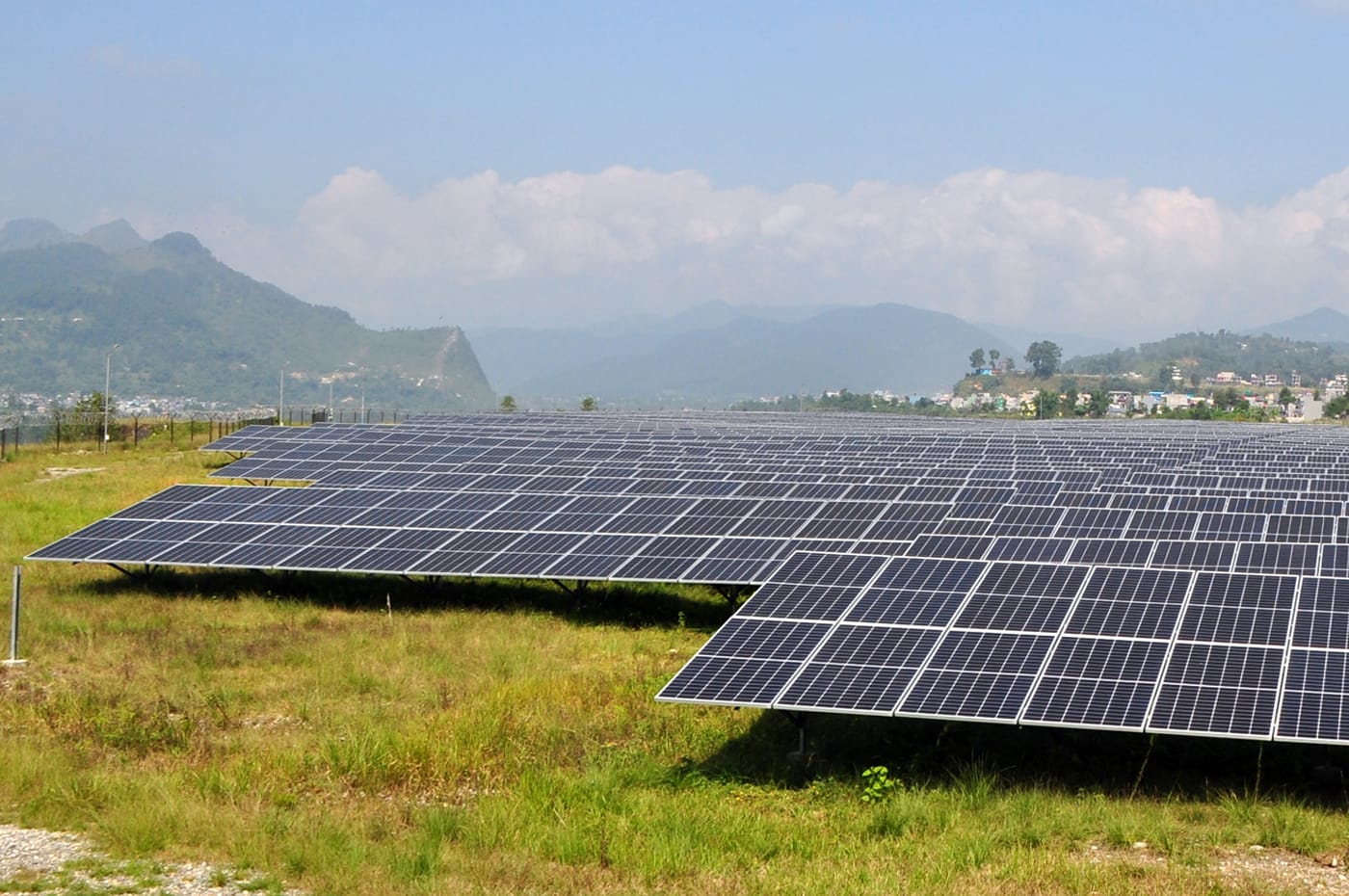 Solar cells in a grassy field with mountains and clouds in the background