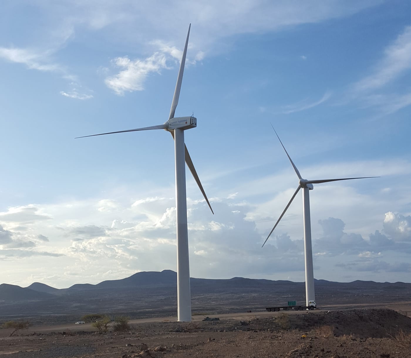 Two wind turbines in front of mountains and a blue sky