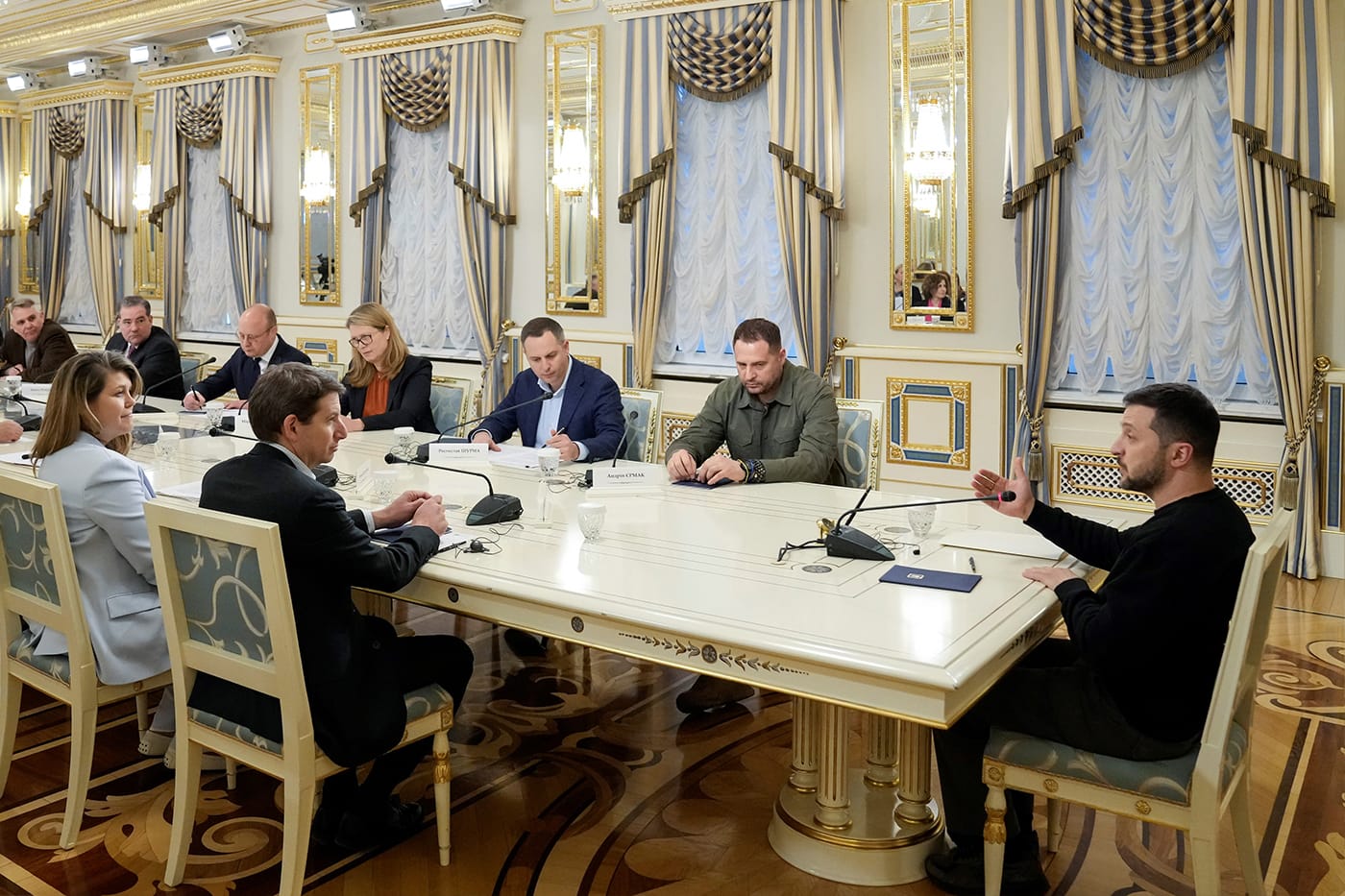Volodomyr Zelenskyy speaking in front of a group of people at a large table